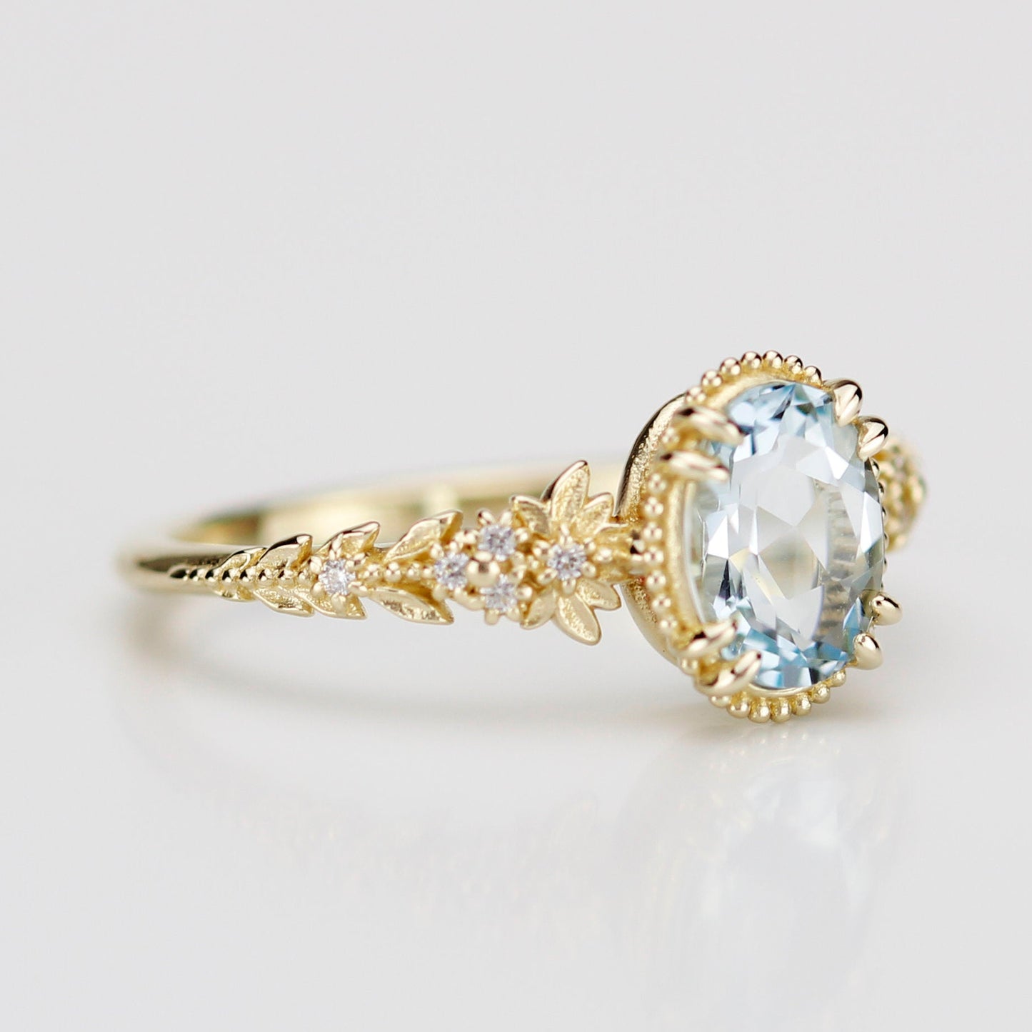 Side view of an 18k gold engagement ring featuring an oval-cut natural aquamarine in a milgrain bezel with a diamond-accented leaf and floral band.