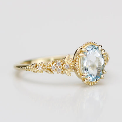 Side view of an 18k gold engagement ring featuring an oval-cut natural aquamarine in a milgrain bezel with a diamond-accented leaf and floral band.