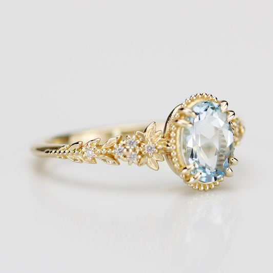 Side view of an 18k gold engagement ring featuring an oval-cut natural aquamarine in a milgrain bezel with a diamond-accented leaf and floral band.