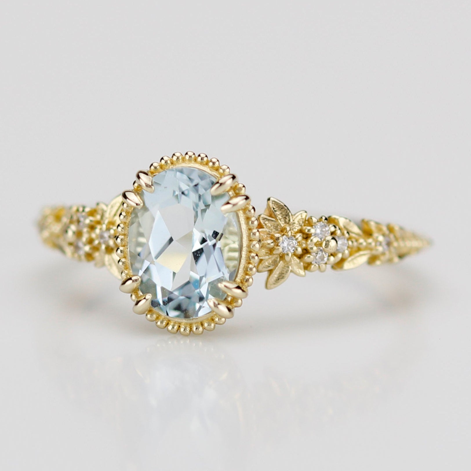 Side view of an 18k gold engagement ring featuring an oval-cut natural aquamarine in a milgrain bezel with a diamond-accented leaf and floral band.