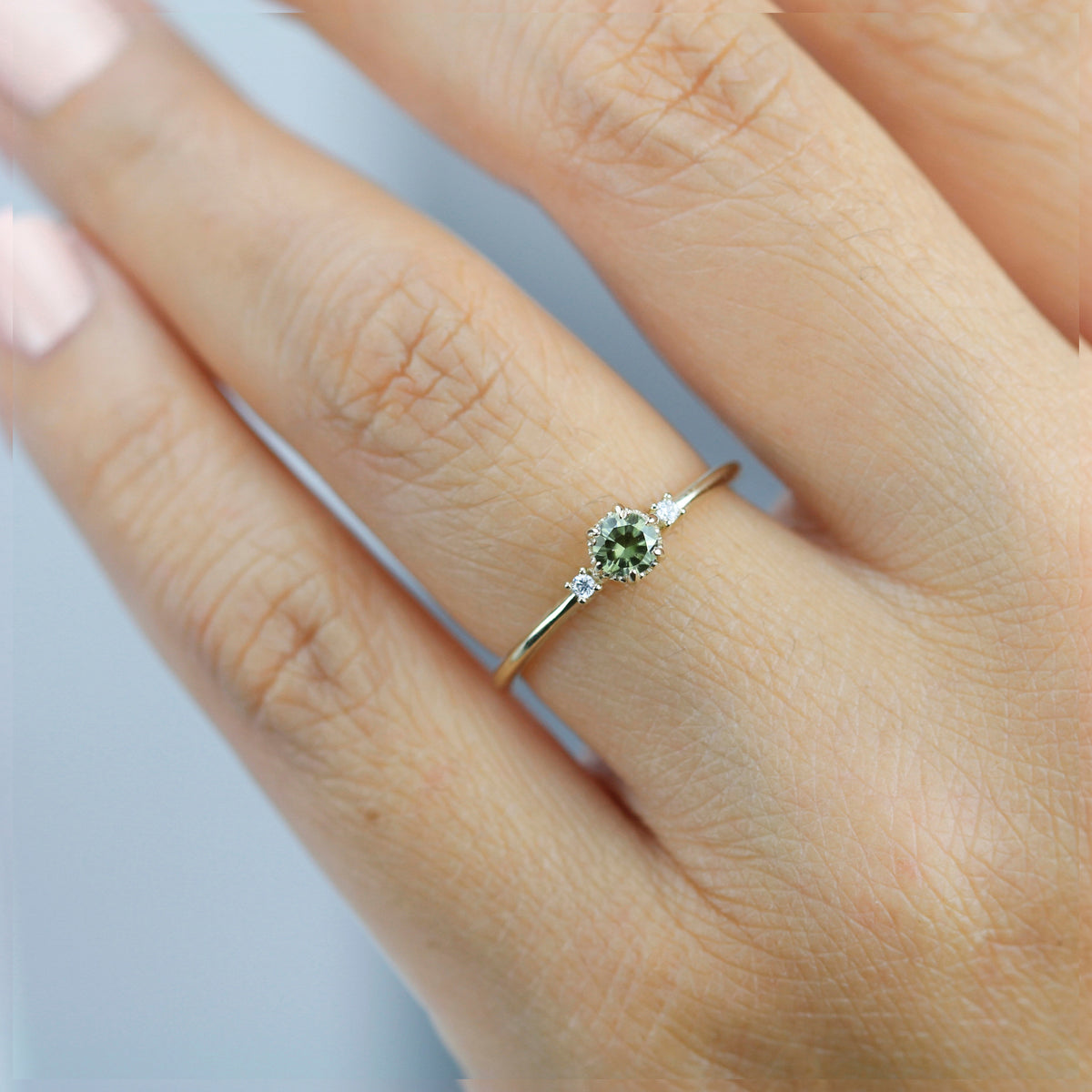 Yellow gold three-stone ring with a green sapphire and two diamonds, worn on a finger