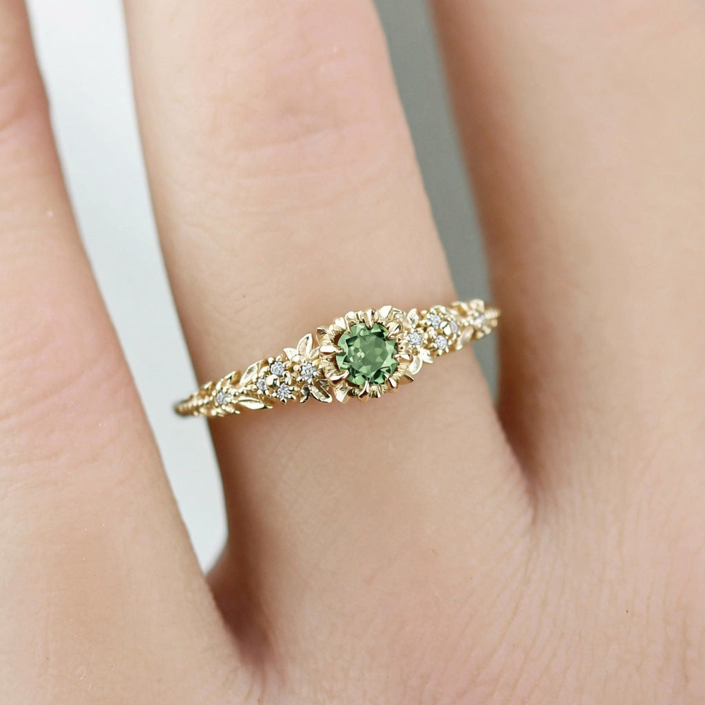 Awen floral ring with a green sapphire and white diamonds, worn on a finger