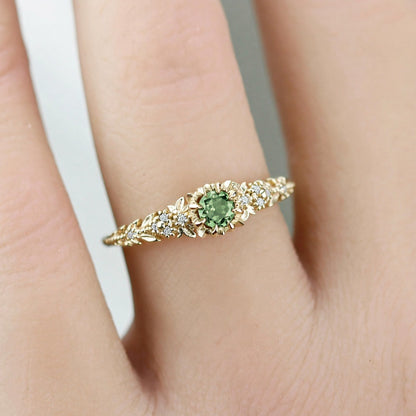 Awen floral ring with a green sapphire and white diamonds, worn on a finger