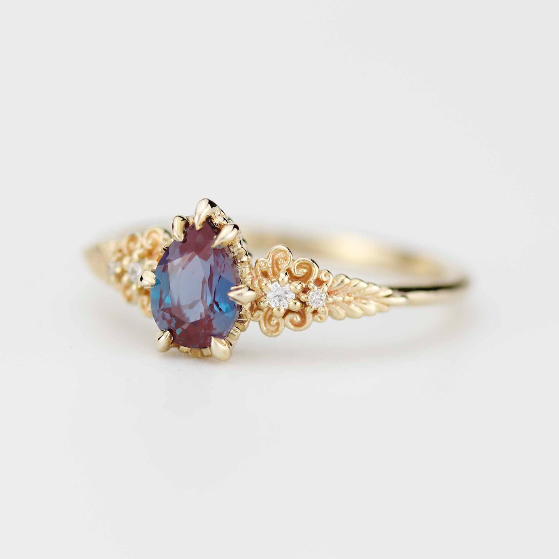 Elegant Nooi Jewelry gold ring featuring an oval-cut bi-color gemstone in red and blue tones, set in prongs with intricate filigree detailing and small accent diamonds along the band.