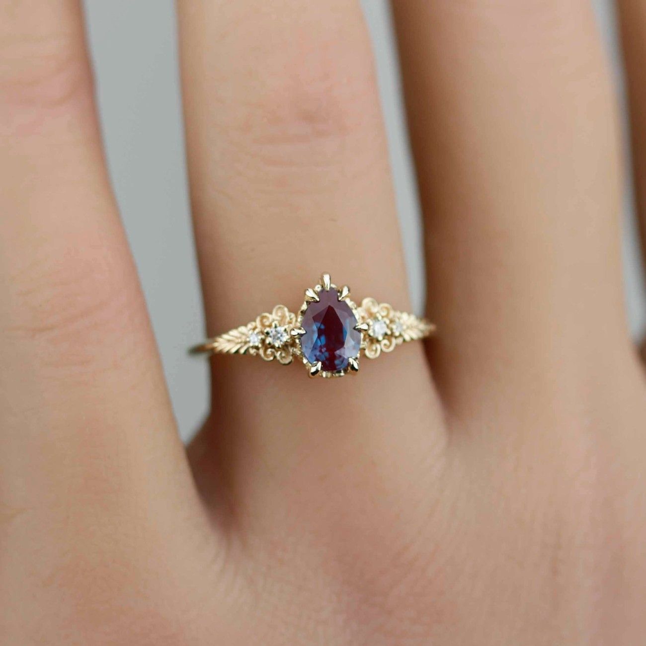 Delicate Nooi Jewelry gold ring featuring a pear-shaped deep red gemstone, accented with intricate filigree details and small side stones, worn elegantly on a finger.