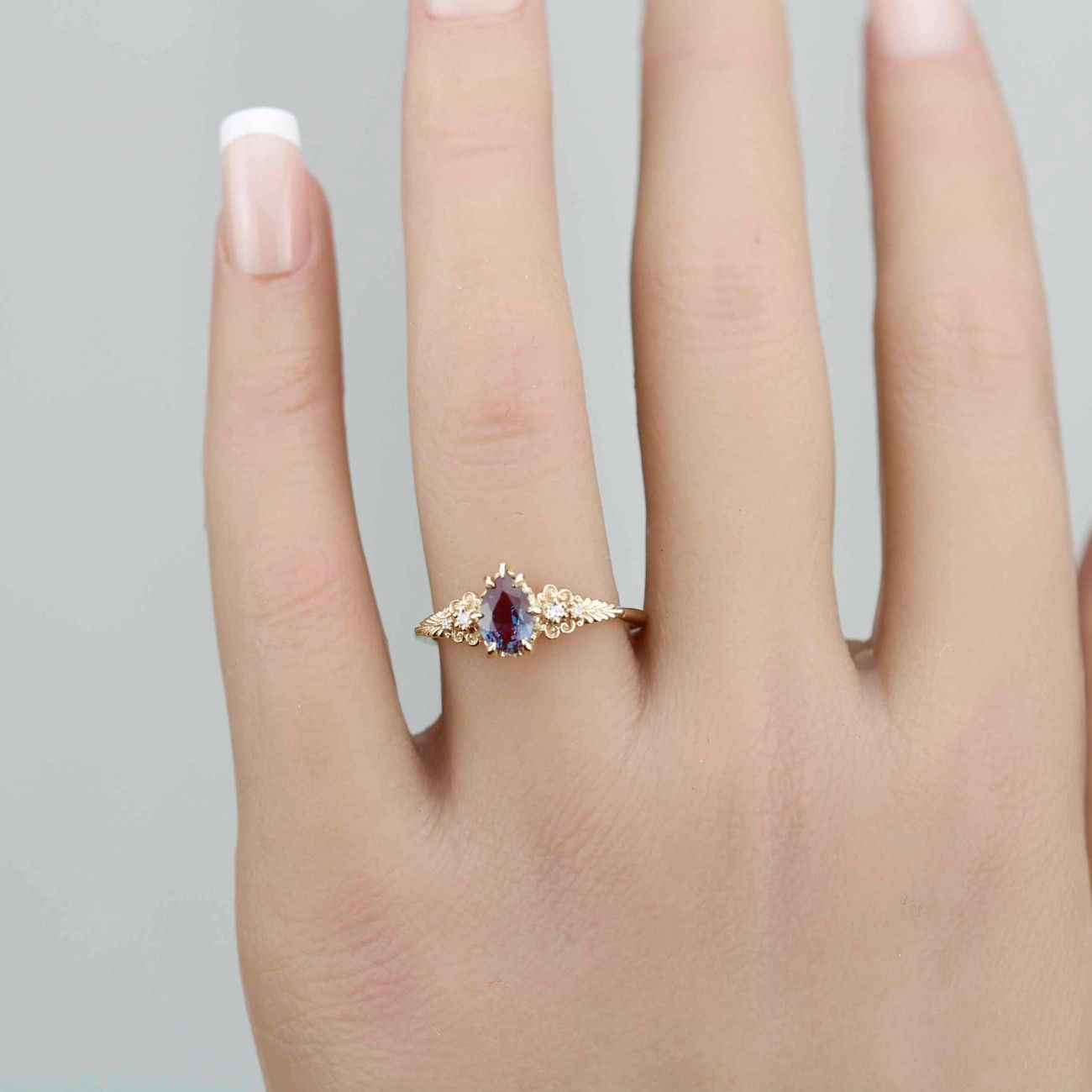 Nooi Jewelry delicate gold ring worn on hand, featuring an oval bi-color gemstone in red and blue hues with intricate filigree detailing and small accent diamonds on the band.