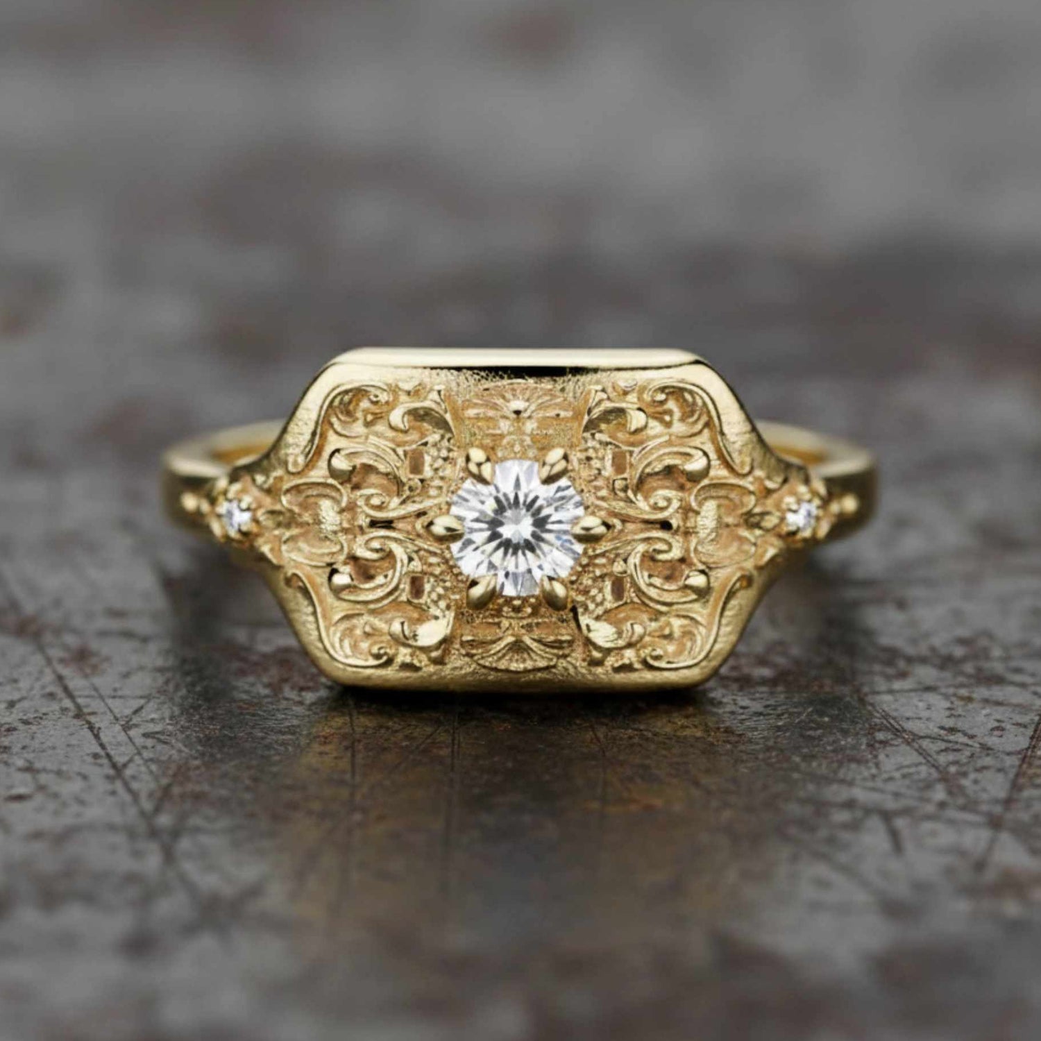 Unisex 18K yellow gold signet ring featuring a rectangular face with deep Victorian scrollwork and a centered natural diamond.