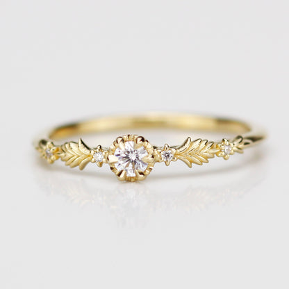18k yellow gold Florisia ring featuring a central 3mm natural white diamond in a textured setting flanked by intricate gold leaf patterns and four tiny accent diamonds on a clean white reflective surface.