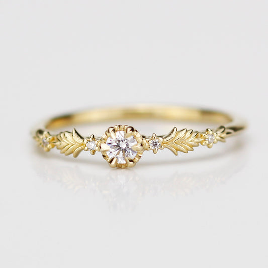 18k yellow gold Florisia ring featuring a central 3mm natural white diamond in a textured setting flanked by intricate gold leaf patterns and four tiny accent diamonds on a clean white reflective surface.
