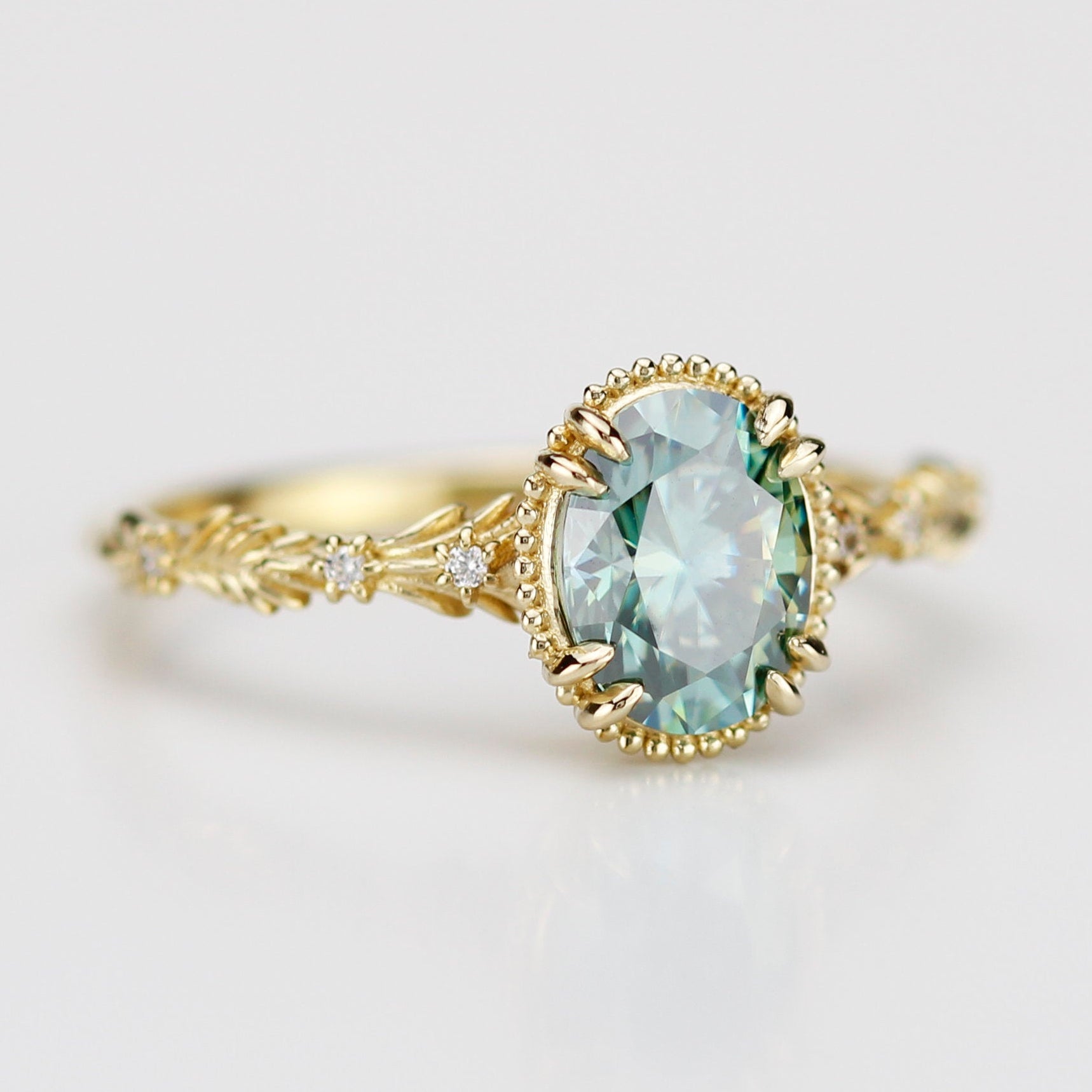 Side view of Rosmaris vintage gold ring featuring an oval green moissanite gemstone in a milgrain bezel with leaf-shaped botanical band and diamonds.