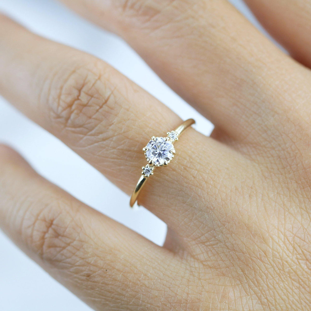 18k gold three stone ring with a round lab grown diamond, worn on the hand, farther view