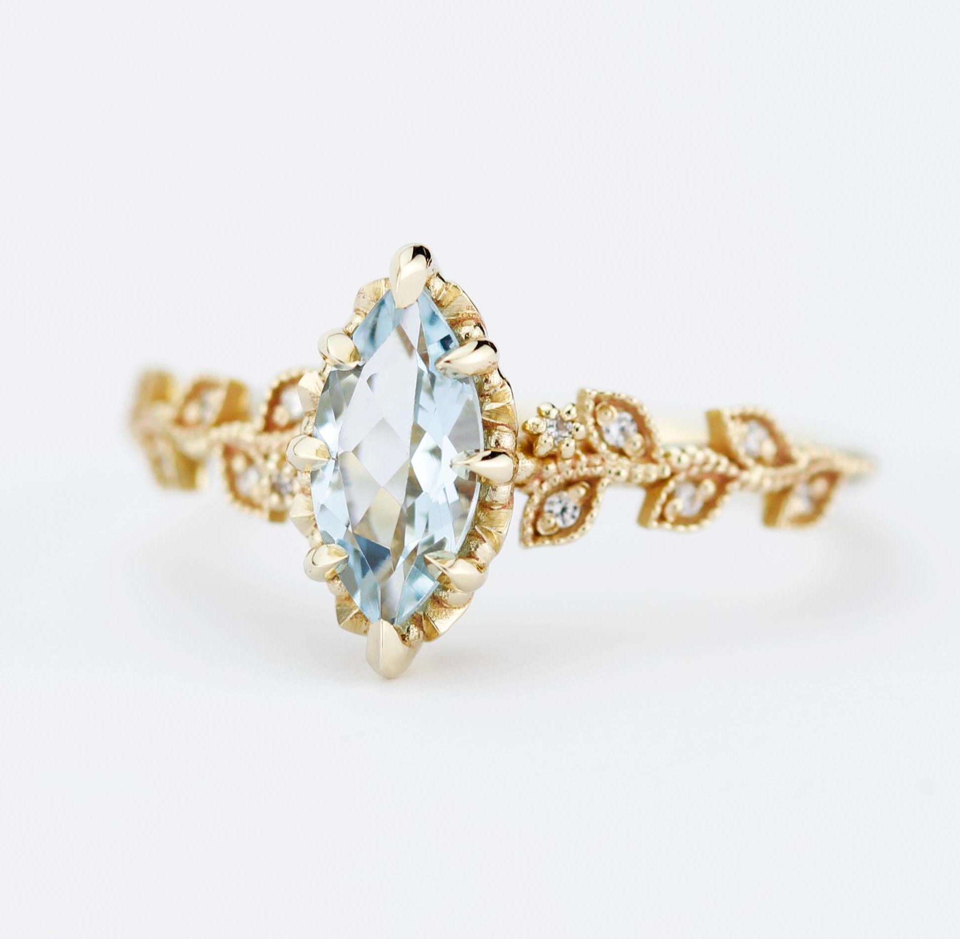 Luxurious ring featuring an 18k solid gold band with a marquise-cut aquamarine gemstone (10x5 mm) at the center. The band is adorned with intricate leaf designs, set with small diamonds, and delicate filigree details