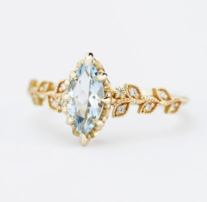 Luxurious ring featuring an 18k solid gold band with a marquise-cut aquamarine gemstone (10x5 mm) at the center. The band is adorned with intricate leaf designs, set with small diamonds, and delicate filigree details