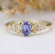 Load image into Gallery viewer, An elegant vintage-inspired 18k yellow gold ring featuring an oval natural blue sapphire as the center piece, accented by sparkling natural diamonds in a delicate floral and scroll design.