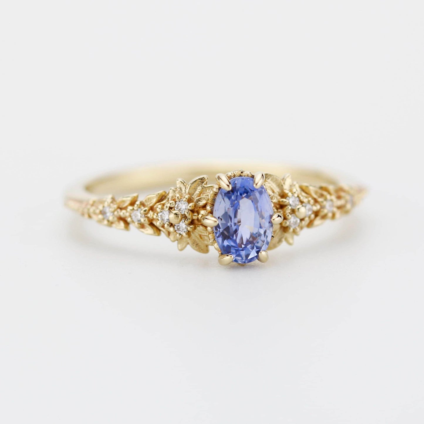 Oval light blue sapphire engagement ring in 18k gold with diamond leaf band and 6-claw setting, handmade nature-inspired design