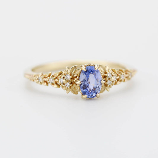 Oval light blue sapphire engagement ring in 18k gold with diamond leaf band and 6-claw setting, handmade nature-inspired design