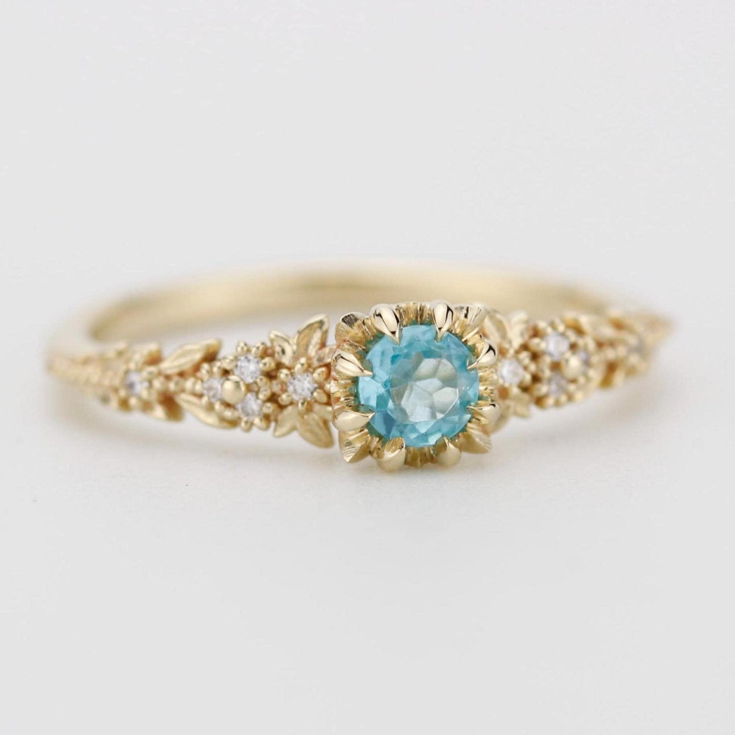 Delicate 18k gold engagement ring with a round blue apatite center stone and diamond accents in a floral setting.
