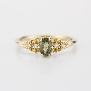 A vintage-inspired 18K gold ring featuring a olive green sapphire, accented with delicate filigree details and natural diamonds, creating an antique-style engagement or heirloom ring.
