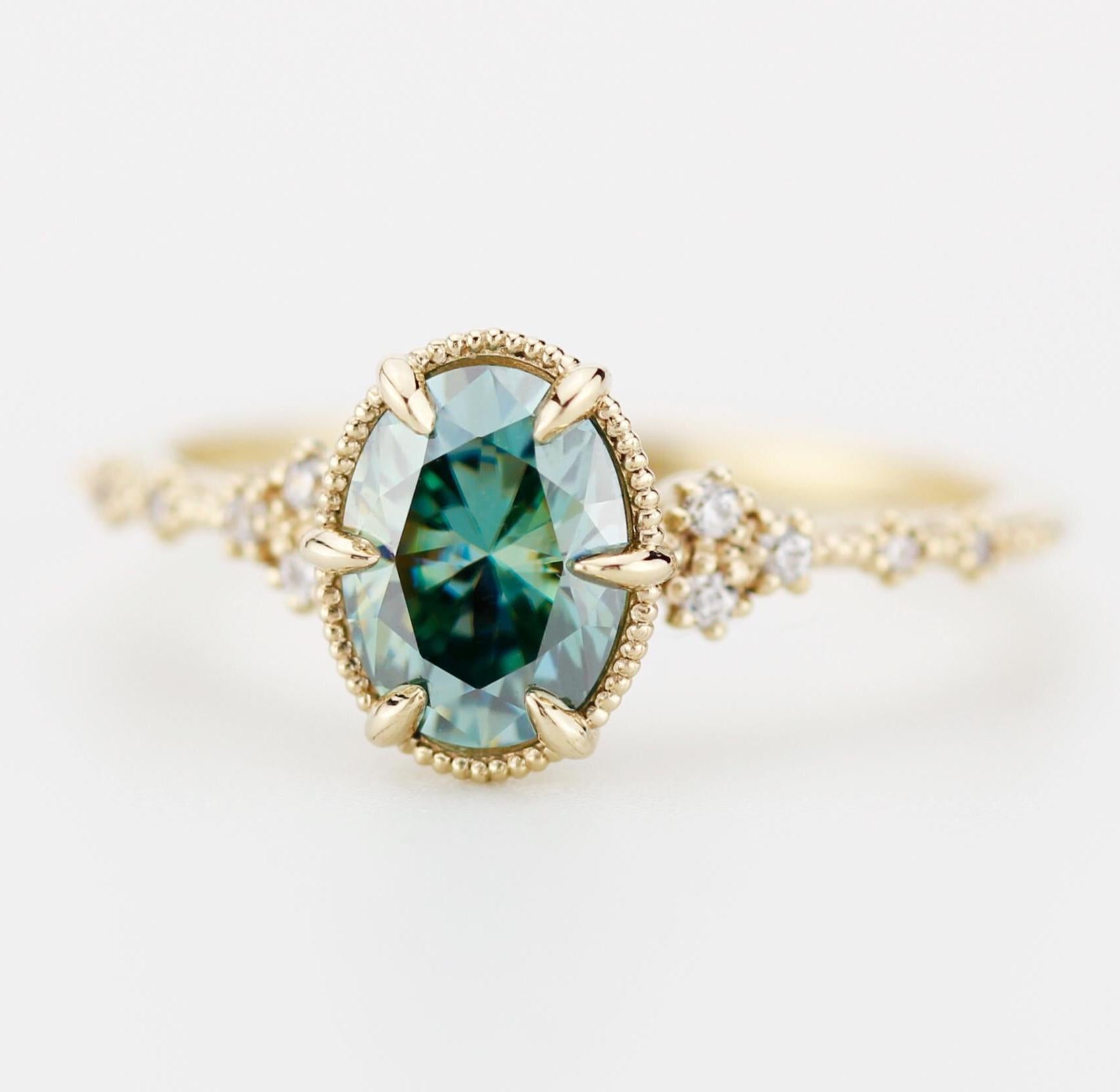 An elegant 8x6 mm teal moissanite gemstone set in an 18k gold band, accented with sparkling diamonds for a refined, luxurious look.