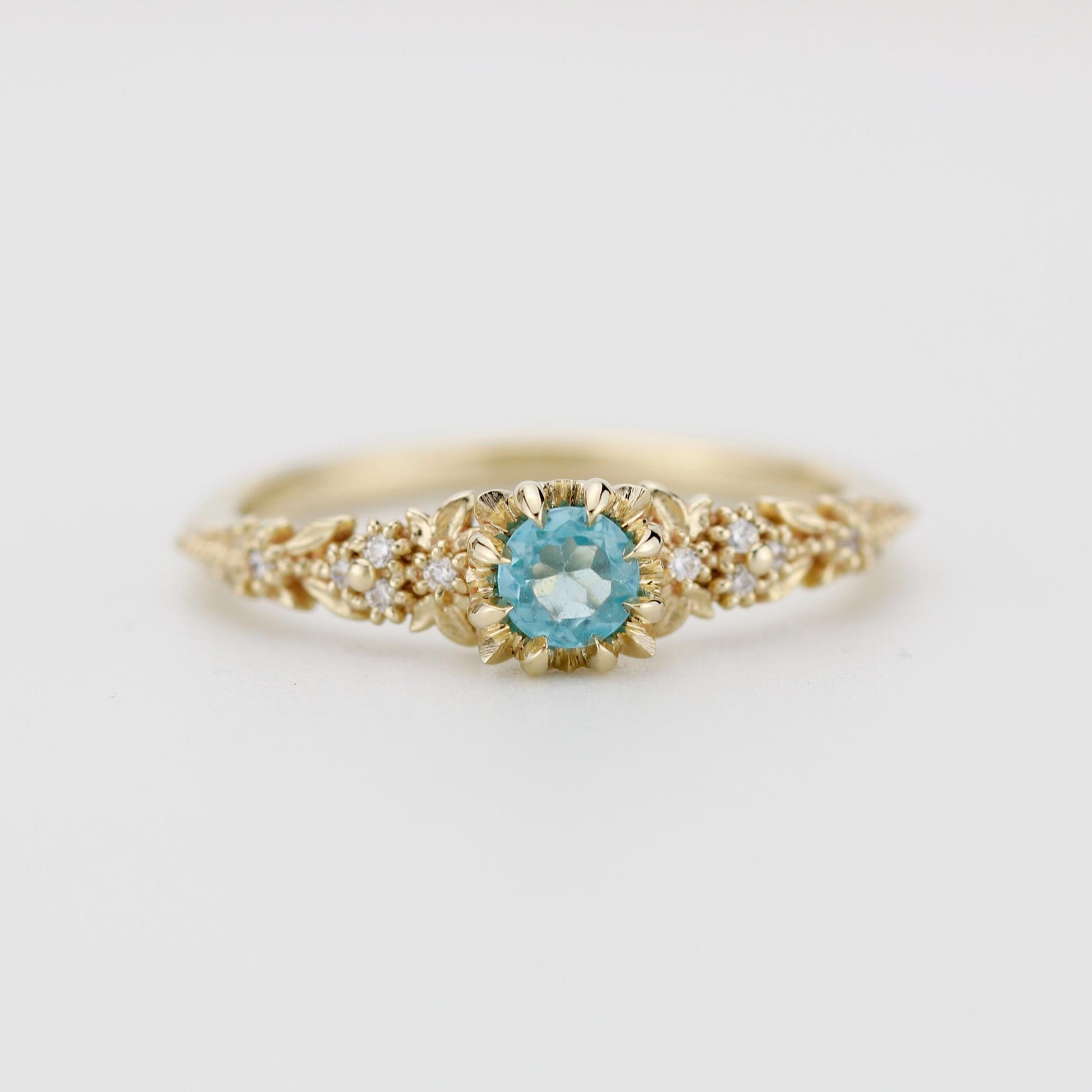 Delicate 18k gold engagement ring with a round blue apatite center stone and diamond accents in a floral setting.