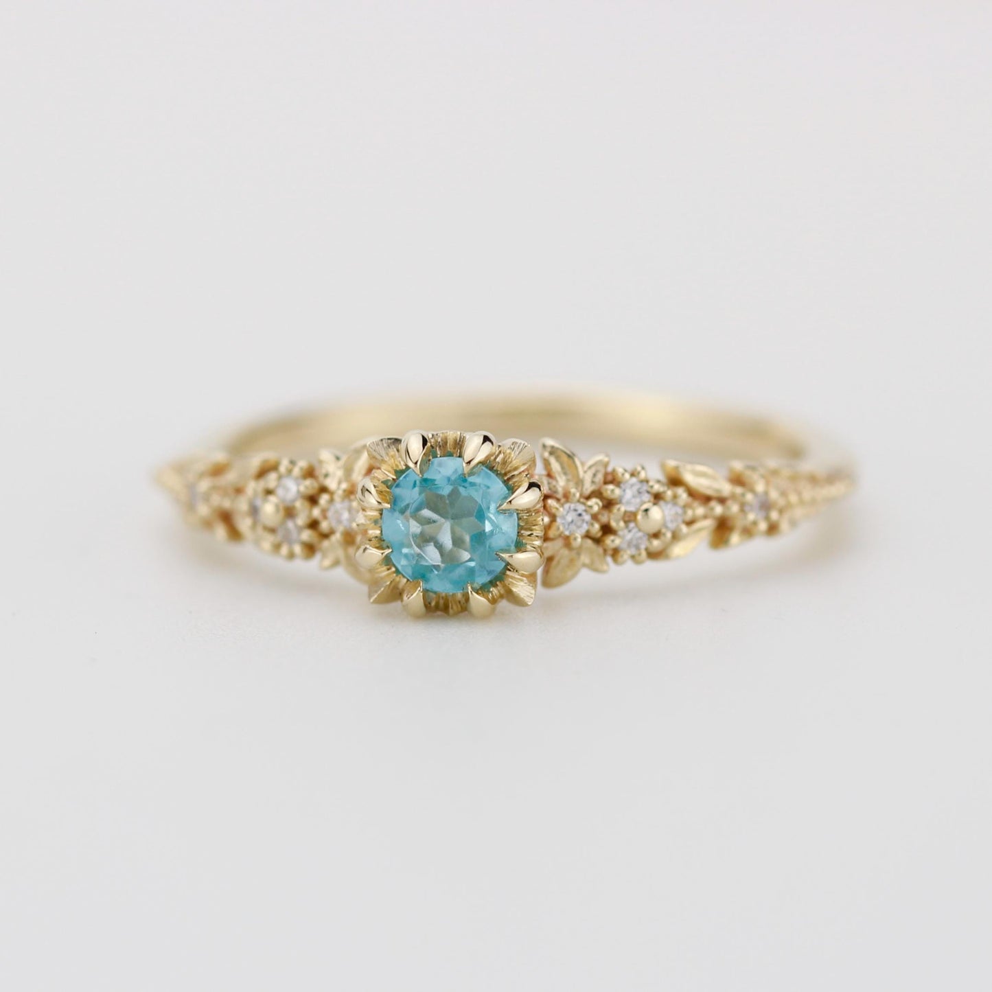 Delicate 18k gold engagement ring with a round blue apatite center stone and diamond accents in a floral setting.