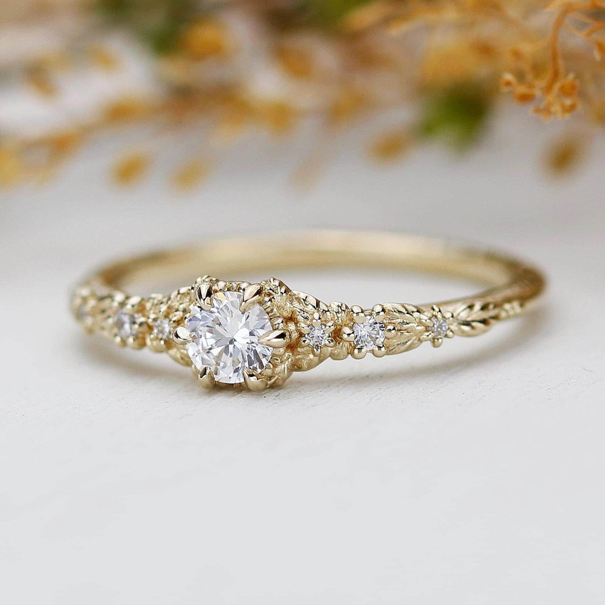 Vintage-inspired 18K gold engagement ring featuring a round natural diamond center stone with intricate leaf detailing and nature-inspired design.