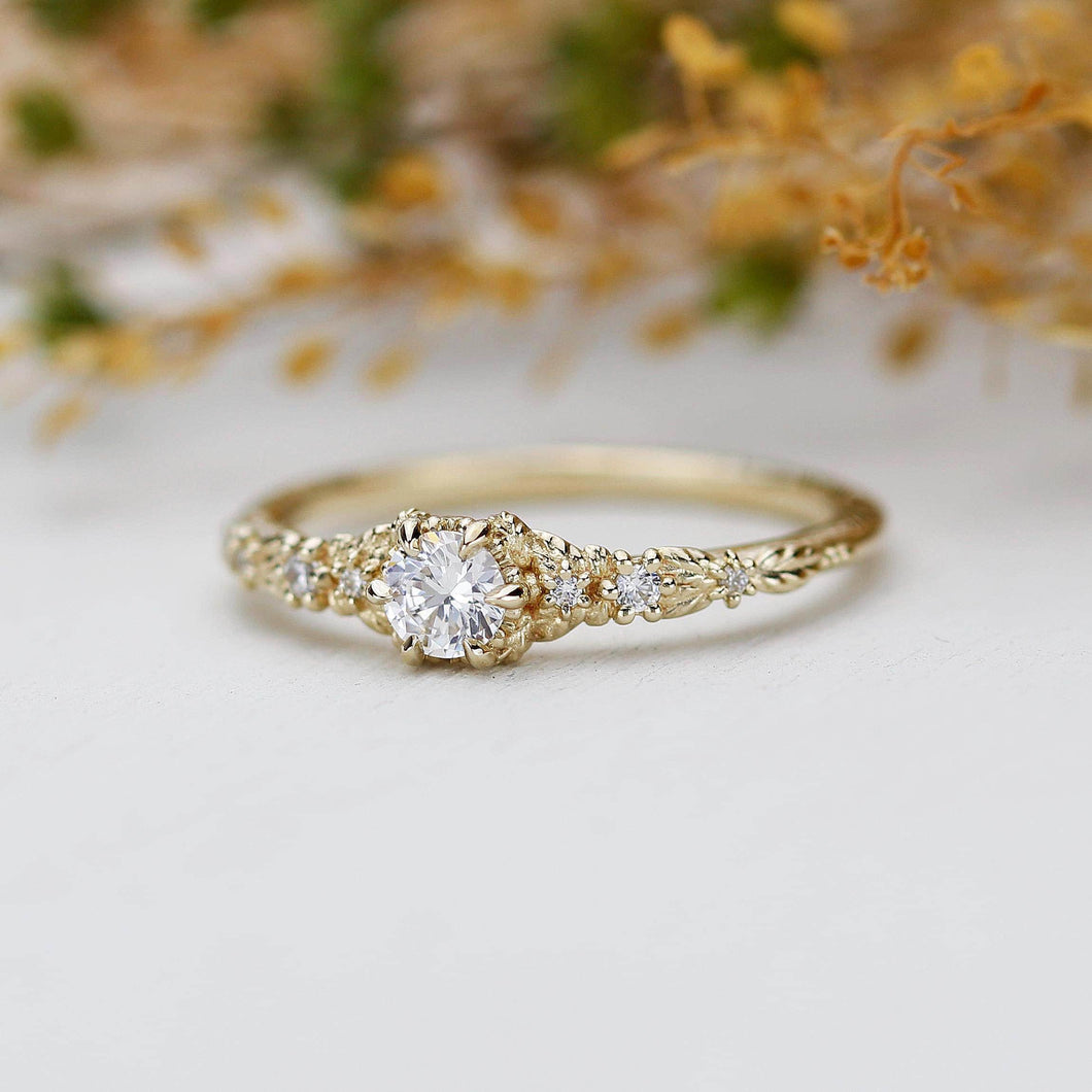 Vintage-inspired 18K gold engagement ring featuring a round natural diamond center stone with intricate leaf detailing and nature-inspired design.