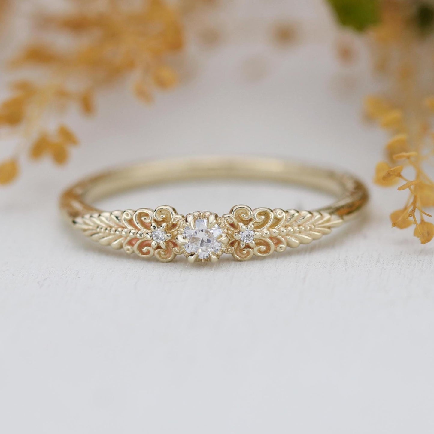 A vintage-inspired 18K gold ring featuring a round natural diamond, accented with delicate scrolls and filigree details and natural diamonds, creating an antique-style engagement or heirloom ring.