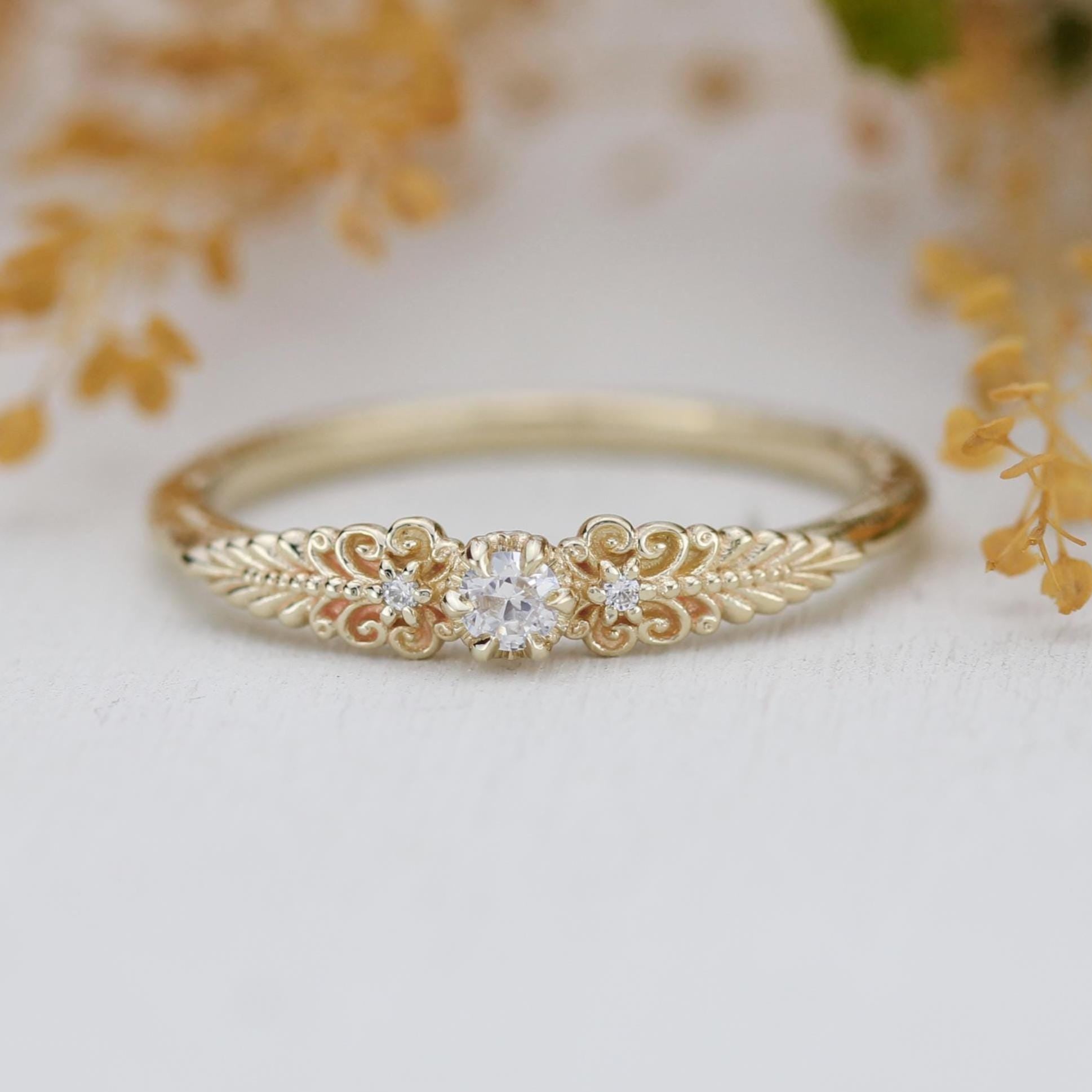 A vintage-inspired 18K gold ring featuring a round natural diamond, accented with delicate scrolls and filigree details and natural diamonds, creating an antique-style engagement or heirloom ring.
