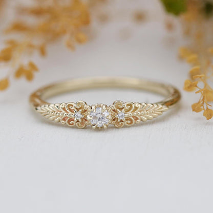 A vintage-inspired 18K gold ring featuring a round natural diamond, accented with delicate scrolls and filigree details and natural diamonds, creating an antique-style engagement or heirloom ring.