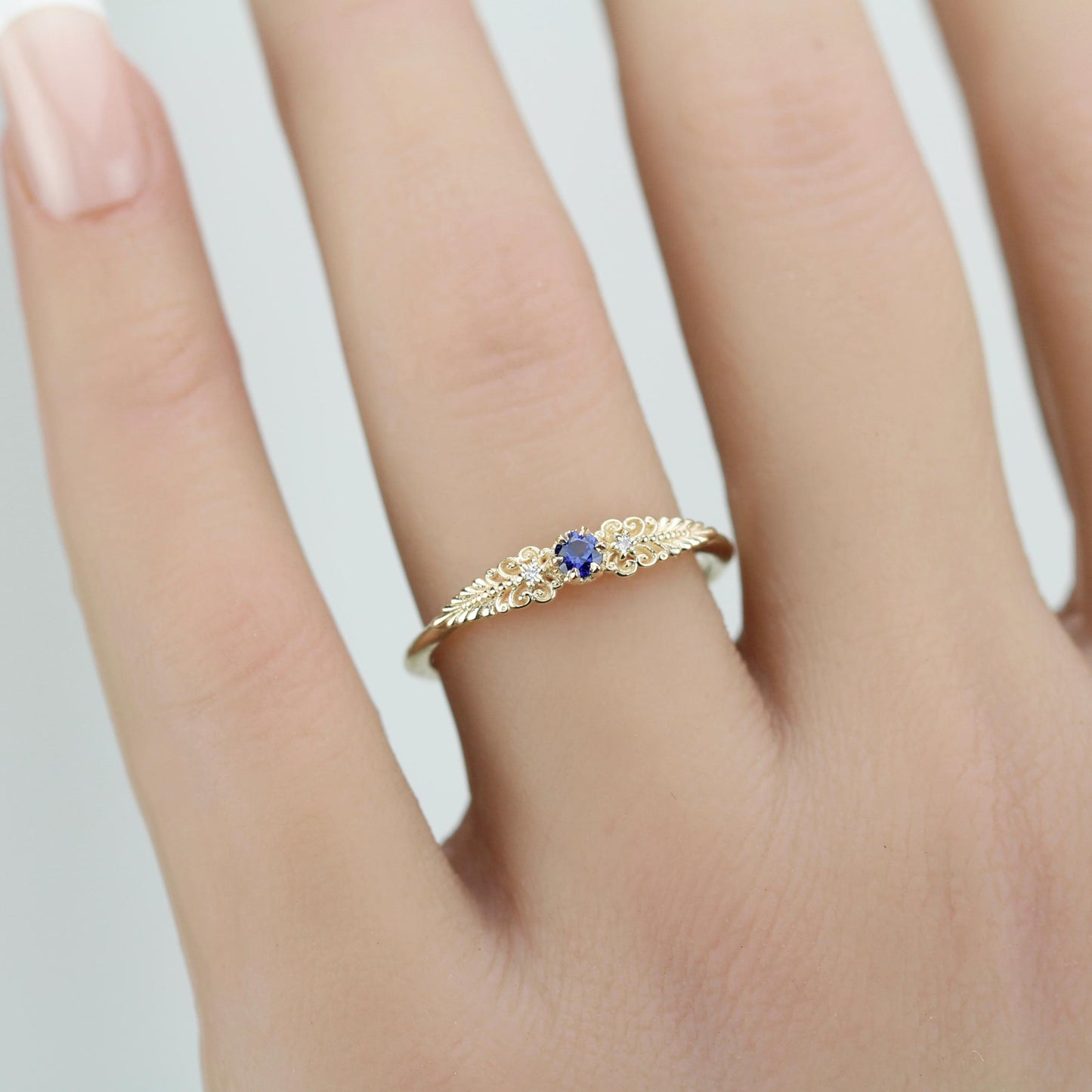 A vintage-inspired 18K gold ring shown on a hand,  featuring a round natural blue sapphire, accented with delicate scrolls and filigree details and natural diamonds, creating an antique-style engagement or heirloom ring.