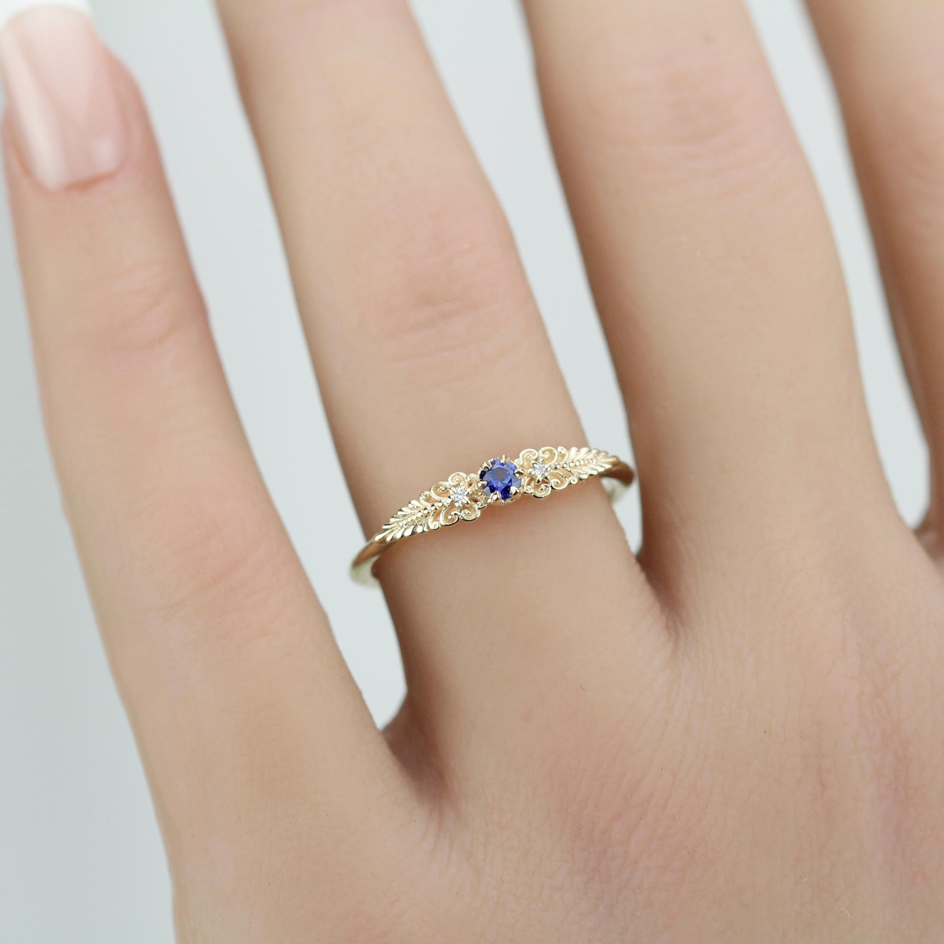 A vintage-inspired 18K gold ring shown on a hand,  featuring a round natural blue sapphire, accented with delicate scrolls and filigree details and natural diamonds, creating an antique-style engagement or heirloom ring.