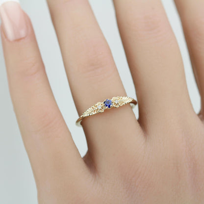 A vintage-inspired 18K gold ring shown on a hand,  featuring a round natural blue sapphire, accented with delicate scrolls and filigree details and natural diamonds, creating an antique-style engagement or heirloom ring.