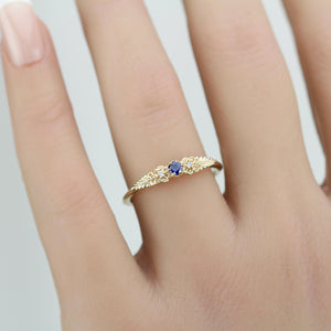 A vintage-inspired 18K gold ring shown on a hand,  featuring a round natural blue sapphire, accented with delicate scrolls and filigree details and natural diamonds, creating an antique-style engagement or heirloom ring.