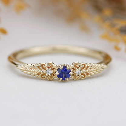 A vintage-inspired 18K gold ring featuring a round natural blue sapphire, accented with delicate scrolls and filigree details and natural diamonds, creating an antique-style engagement or heirloom ring.