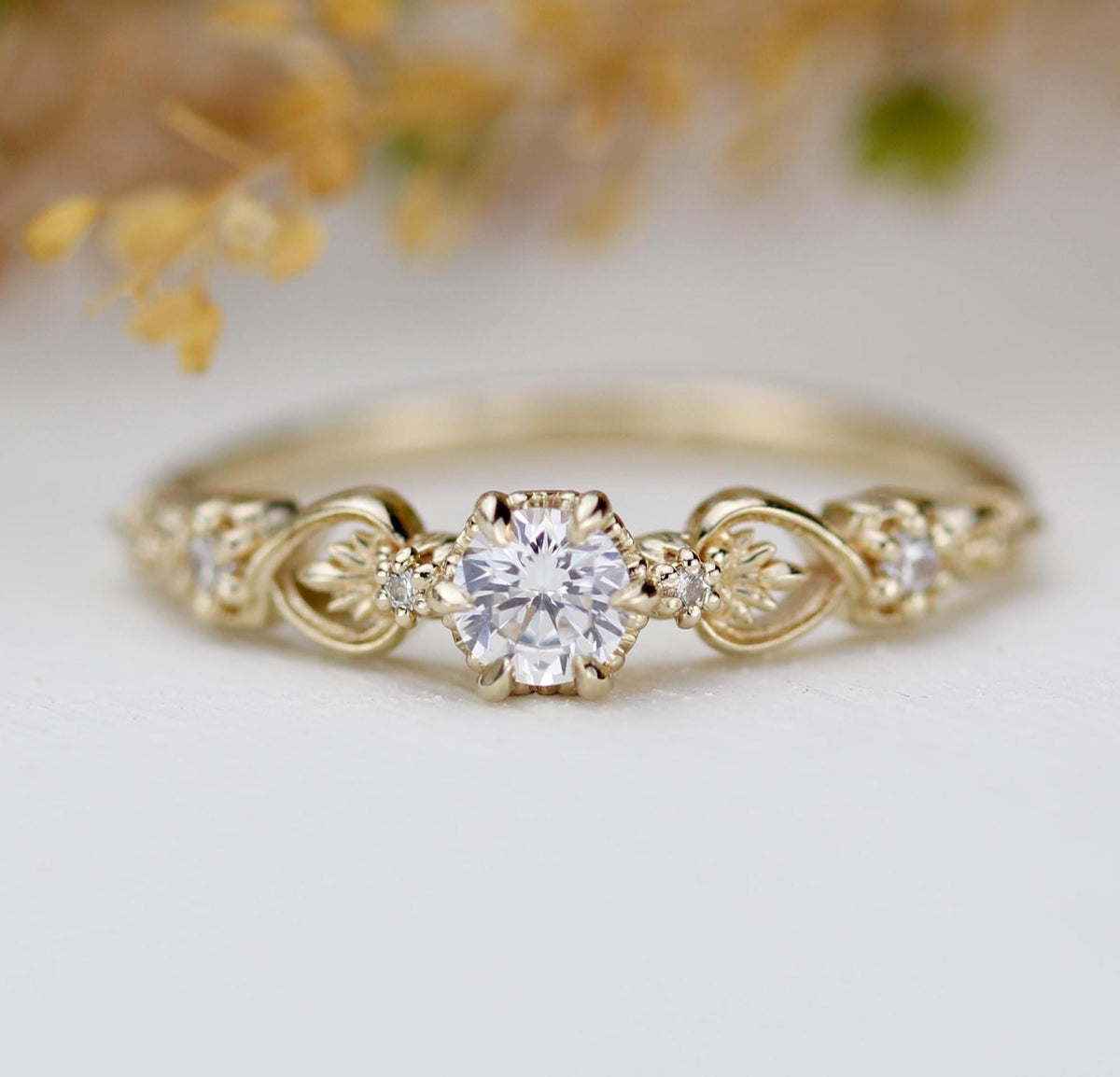 18k gold baroque scroll ring with a round lab grown diamond, dried flowers behind