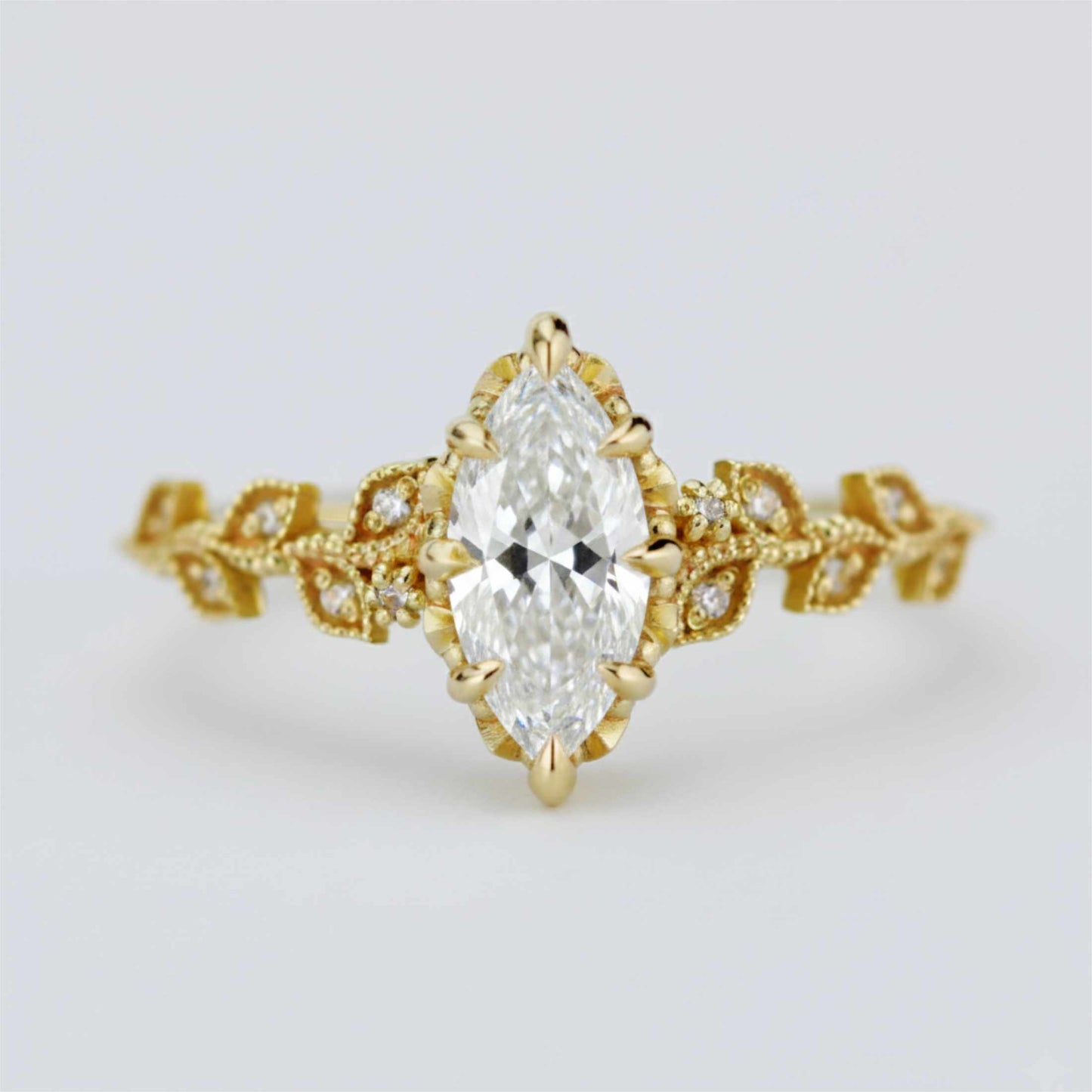 Elegant Nooi Jewelry engagement ring featuring a marquise-cut diamond in a gold setting with intricate leaf-inspired band and delicate pavé diamond accents.