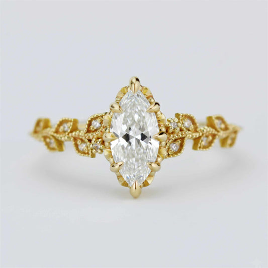 Elegant Nooi Jewelry engagement ring featuring a marquise-cut diamond in a gold setting with intricate leaf-inspired band and delicate pavé diamond accents.