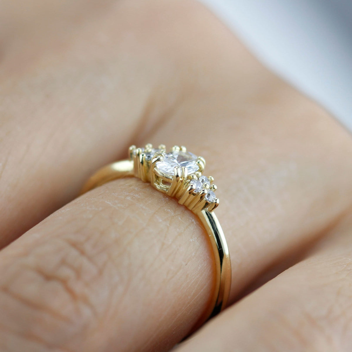 18k gold cluster ring with an oval lab grown diamond, worn on the hand, side view